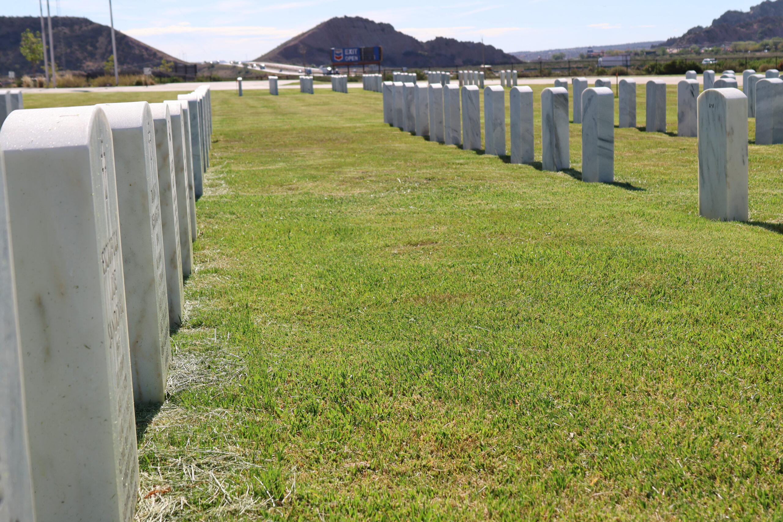 Grassy lawn with evenly spaced, grey markers and low hills in the distance.